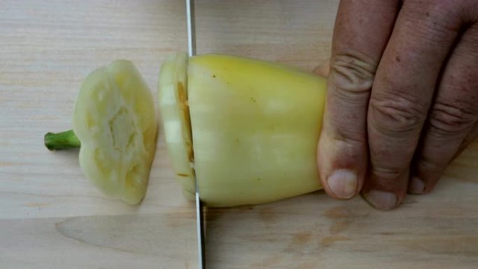 自制烹饪。人的手用锋利的菜刀切了一个甜美的铃铛黄椒。