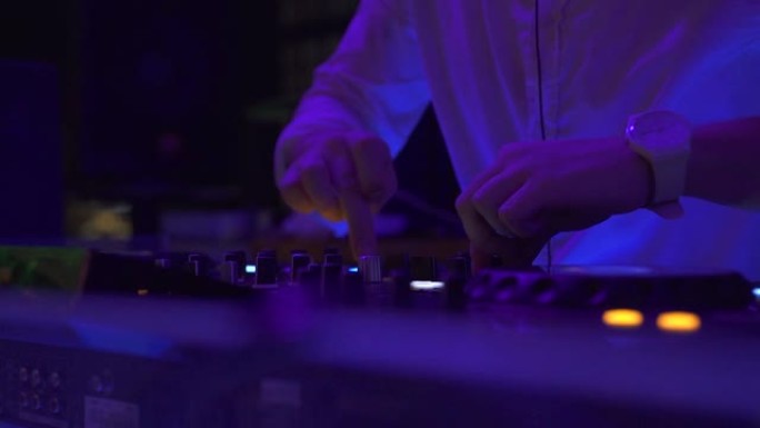 男子DJ在夜总会派对上在音响控制台播放舞蹈音乐。DJ控制器，用于在夜总会混合音乐和彩色灯光。舞会上的