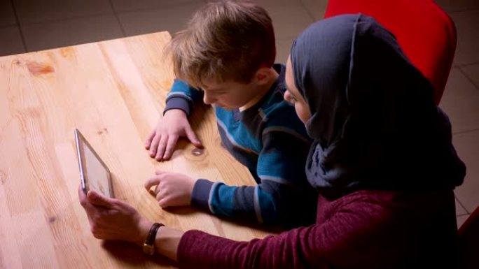 小男孩和他的穆斯林母亲戴着头巾在平板电脑上观看动画片的个人资料。
