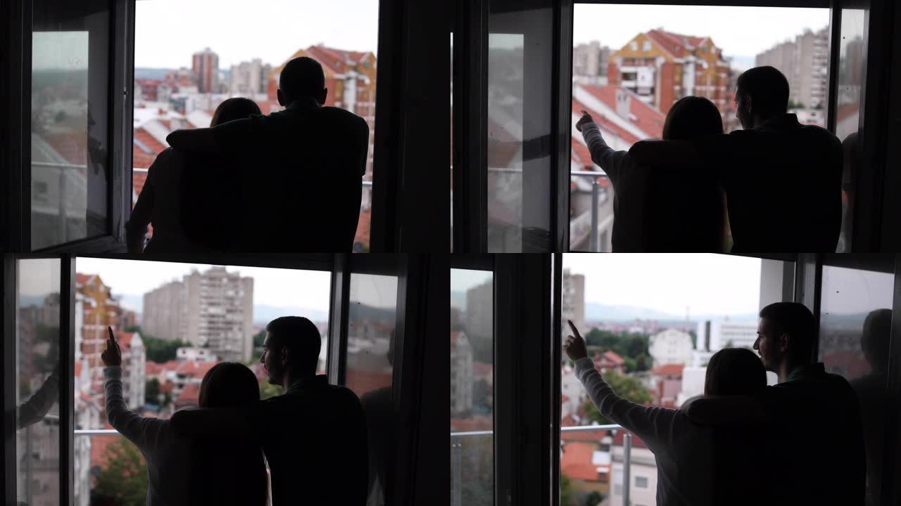幸福的夫妇拥抱着，看着他们新公寓的窗户