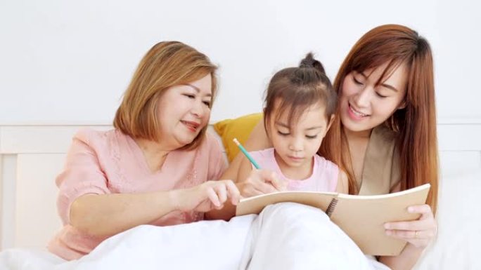 亚洲的母亲和母亲在卧室教女儿写作。