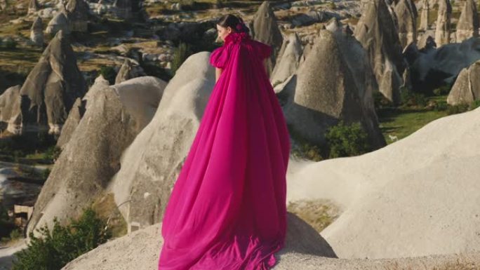 穿着紫色长裙的女孩站在卡帕多西亚的一块岩石上