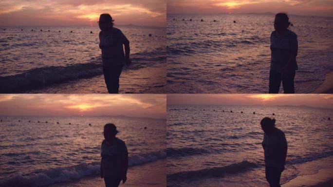 在日落/日出背景下沿着海滩散步的高级女性