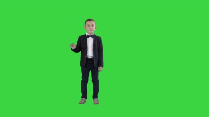 穿着西装的友好小男孩打招呼，然后在绿色屏幕上说再见，色度键