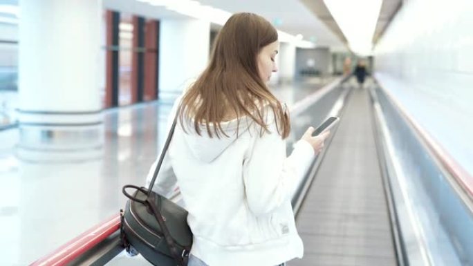 背面视图欧洲妇女在国际机场移动人行道上通过电话发短信