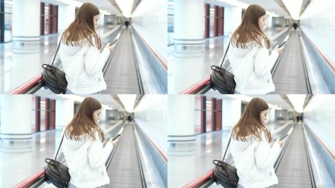 背面视图欧洲妇女在国际机场移动人行道上通过电话发短信