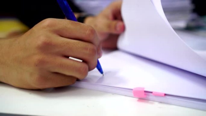文件报告和业务繁忙的概念:商人经理手握蓝色钢笔阅读和签署文件或文件文件的电脑现代公司办公背景。