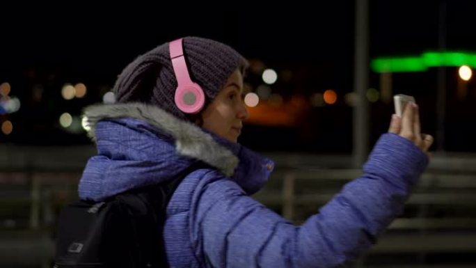 女孩在夜镇的街道上散步时使用手机进行视频通话