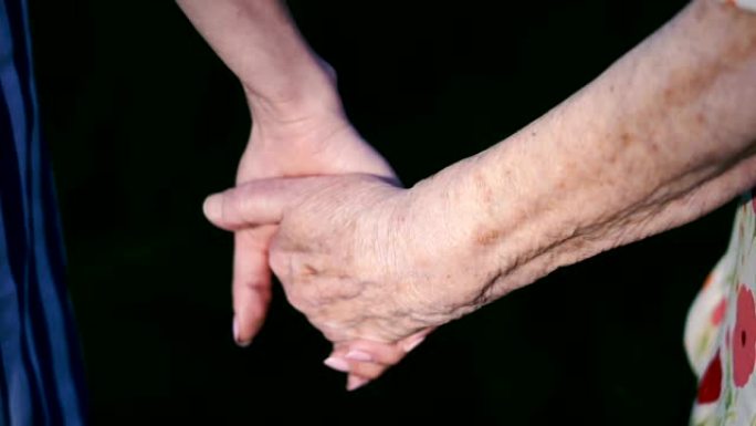 手臂。祖母的旧手握住年轻女性的手