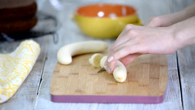 女人在砧板上切香蕉的特写。在砧板上的木桌上，一个女人用刀切成香蕉。