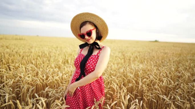 麦田时尚女人的肖像。穿着草帽、心形眼镜、红色圆点连衣裙和口红的老式女孩。旅游、时尚、自然概念