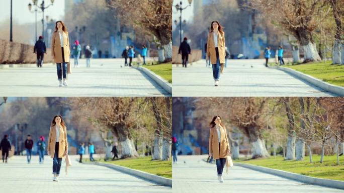 优雅的年轻女子在早春穿过公园。人和孩子走路，鸟儿飞。摄像机的圆周运动。