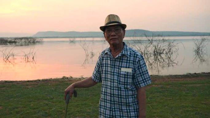 高级亚洲男性的场景慢动作是站在手杖上欣赏湖边的自然风光，他在假期，放松的时刻很开心，很开心。户外自然
