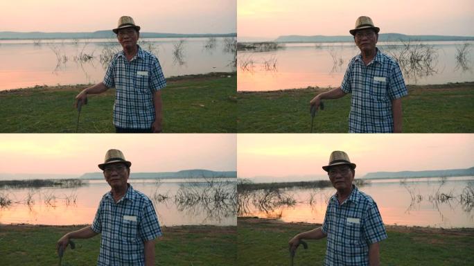 高级亚洲男性的场景慢动作是站在手杖上欣赏湖边的自然风光，他在假期，放松的时刻很开心，很开心。户外自然