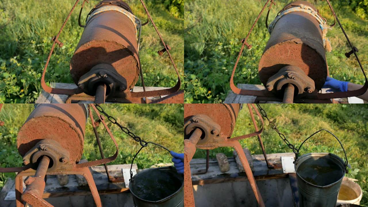 女人用水桶把链子扔进乡村井取水。老式水井链特写。村子里老生锈的铁链。