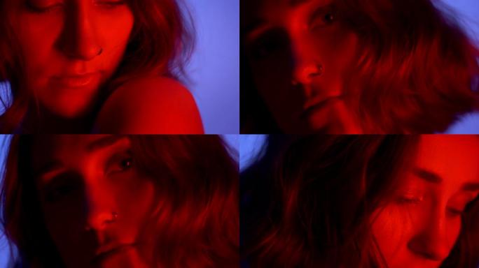 裸露肩膀的年轻迷人高加索女性的特写镜头诱人地看着霓虹蓝色和红色背景的相机