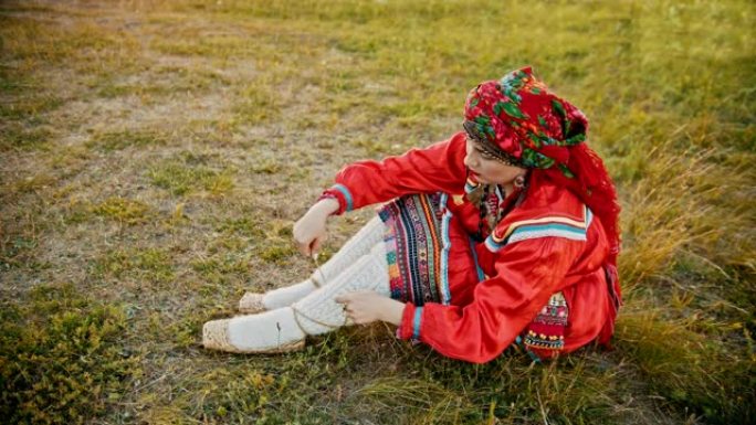 一个穿着俄罗斯红色民衣的女人穿上韧皮鞋-坐在球场上。