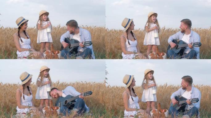 家庭在野外度假，年轻的父亲弹吉他，与妻子在女儿喝酒时大笑，并在小麦谷物作物草甸的户外野餐中舔牛奶胡须