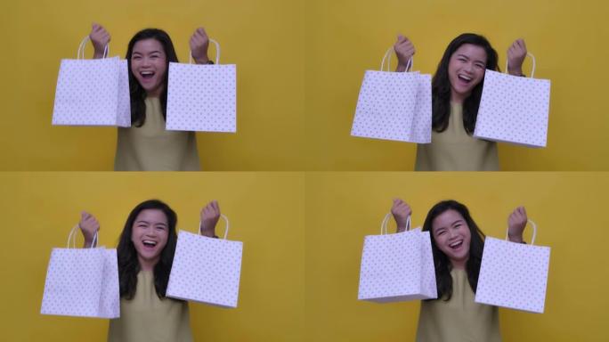 SLO MO拍摄了一个快乐的亚洲女人双手拿着购物袋的黄色背景