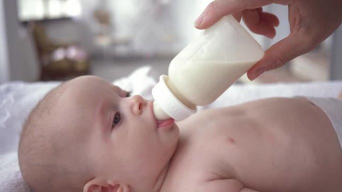 刚出生的婴儿从妈妈手里拿着的瓶子里喝牛奶，在换衣桌上尿布的小女孩的肖像