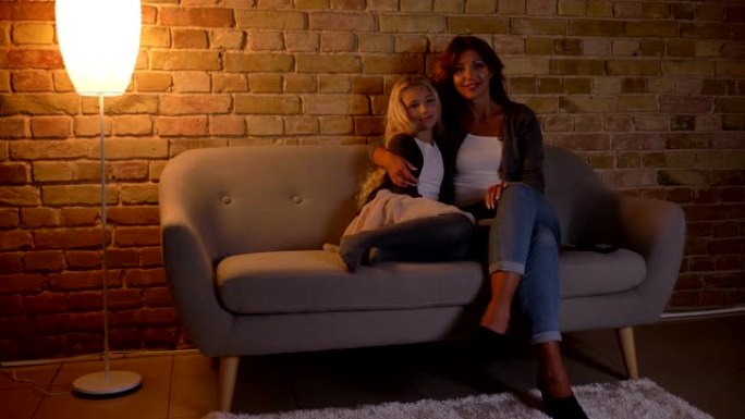 年轻的高加索女性和她的小漂亮女儿坐在沙发上拥抱的特写镜头