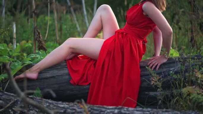 一个穿着红色连衣裙的年轻漂亮的女孩正站在森林里。