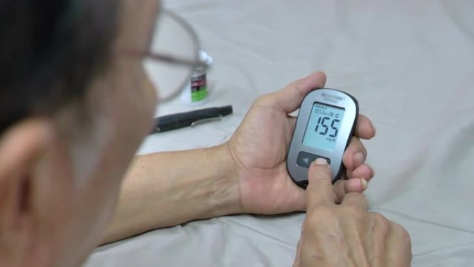 老年亚洲男性糖尿病患者在家中使用血糖仪，查看血糖结果