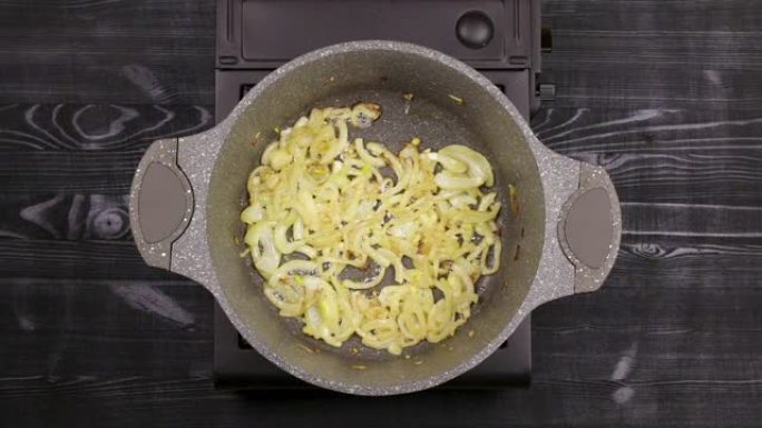 切成薄片的洋葱片在带有大理石或石头不粘涂层的平底锅中烤成金黄色。石油在底部沸腾。顶视图。