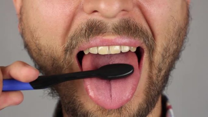 留着胡须和小胡子的男人用黑色牙刷彻底刷舌头，前视图，按摩和清洁牙菌斑，特写