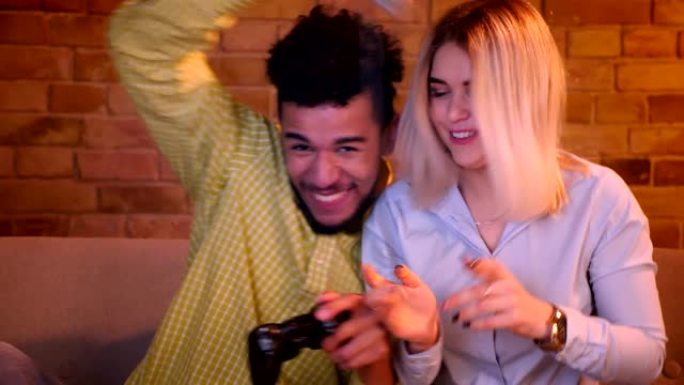 非洲男人和他的金发高加索女友在舒适的家里玩游戏杆玩电子游戏。