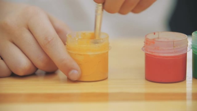 创意男孩正在借助裸色画笔在罐子中混合和搅拌黄色油漆。