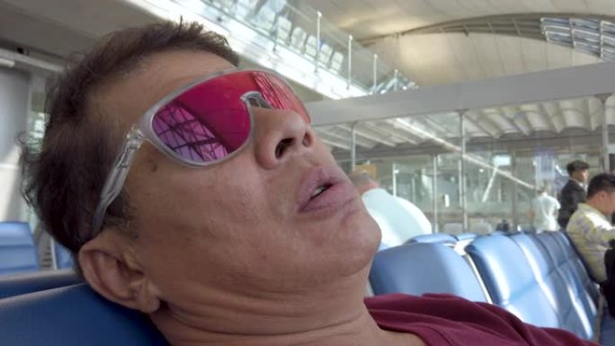 亚洲老人在机场戴着墨镜睡觉。