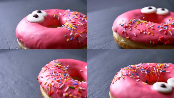 美味的粉红色甜甜圈的特写镜头，上面有彩色的碎屑，眼睛在灰色的桌子背景上缓慢旋转。