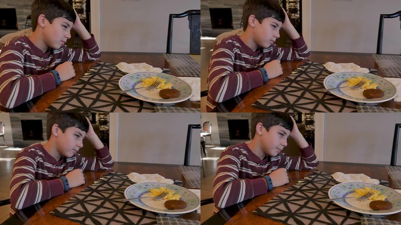 不快乐的年轻8-10岁男孩坐在桌子旁不吃早餐