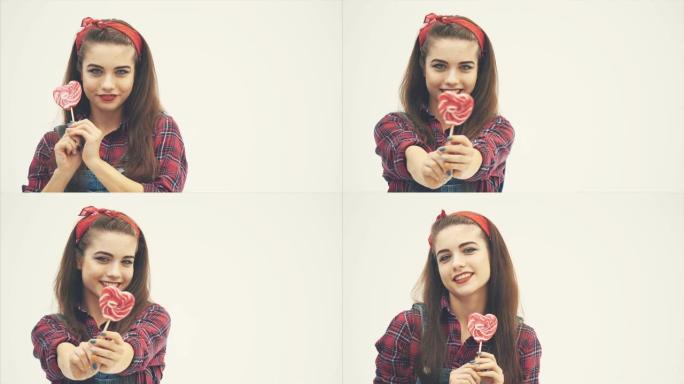 可爱迷人的女孩拿着红色的心形棒棒糖，在镜头前挥舞。