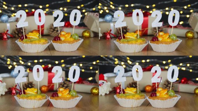 新年快乐糖果土地棒棒糖纸杯蛋糕与2020数字与散景圣诞仙女灯背景。用数字作为新2020年的象征的纸杯