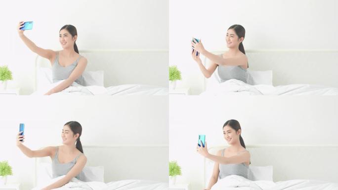 亚洲女性在卧室张贴并拍照，用智能手机拍摄自己的新照片。技术、通信、网络摄像头、上传和自拍的概念。