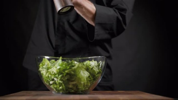 库克将盐和香料洒在黑色背景上的绿色沙拉特上