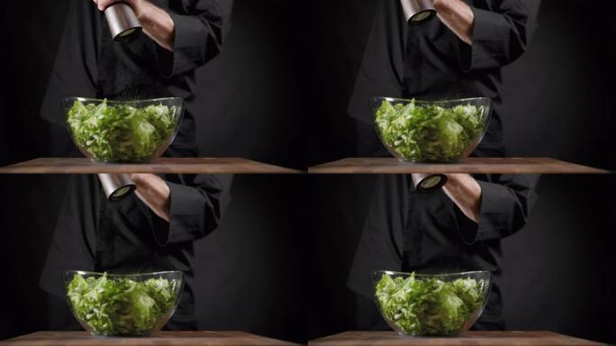 库克将盐和香料洒在黑色背景上的绿色沙拉特上