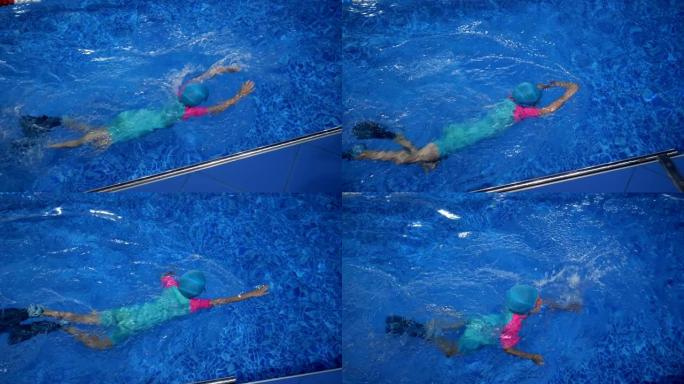 戴着护目镜的游泳帽和脚蹼的女童正在训练游泳池游泳。