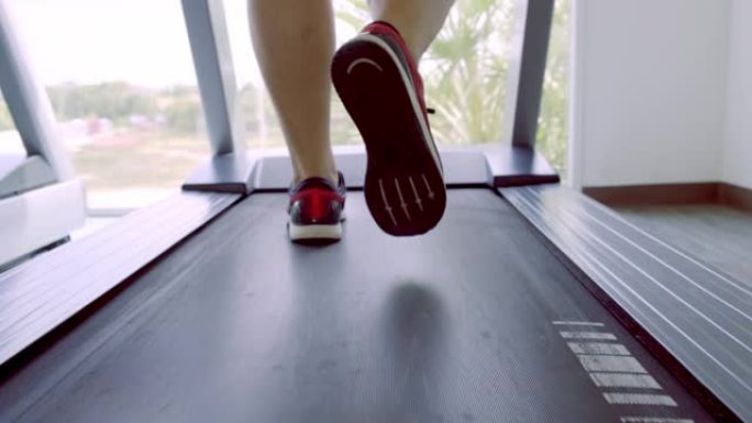 在健身房的跑步机上关闭穿着粉色运动鞋的男人的腿