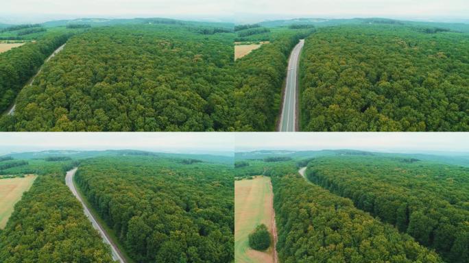 汽车在绿地之间的道路上行驶的鸟瞰图。4k从树林到公路和田野的无缝过渡。