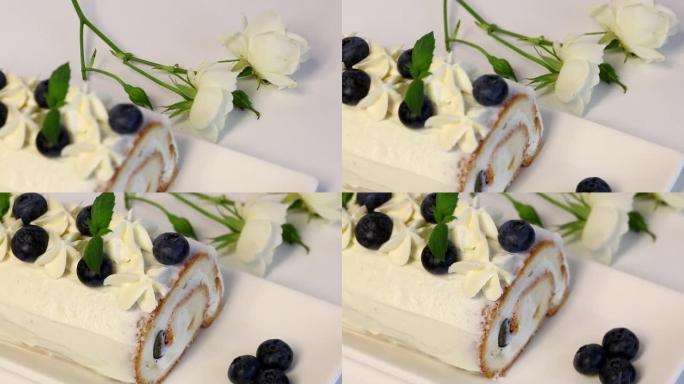 涂有奶油的海绵蛋糕，并饰有蓝莓干和新鲜薄荷叶。附近有一朵白玫瑰。