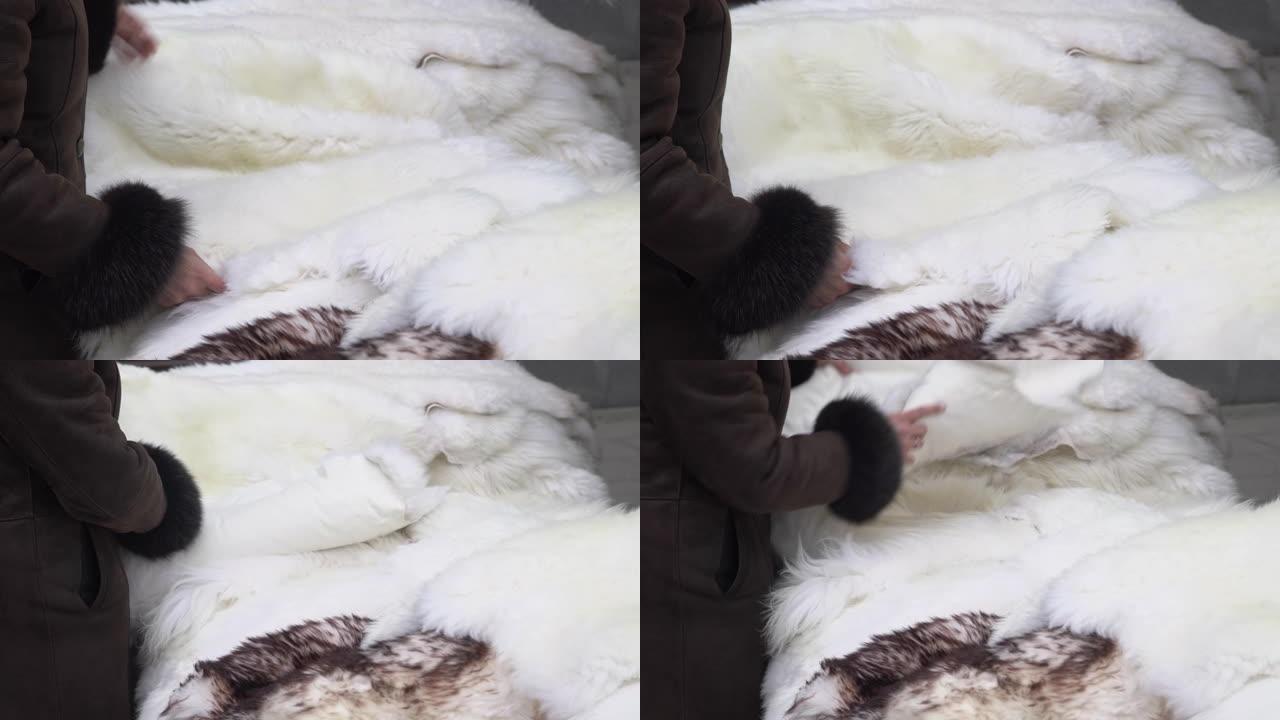 顾客在市场上采摘温暖的冬季羊皮。女人的手选择动物皮垫或地毯在城市街头市场出售