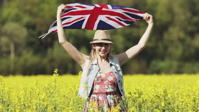 夏天，一个带着英国国旗的快乐迷人的女人在黄色的油菜籽田里跳舞。