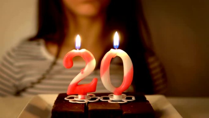 快乐的少女庆祝自己的20岁生日，并在室内自制烤蛋糕上吹蜡烛