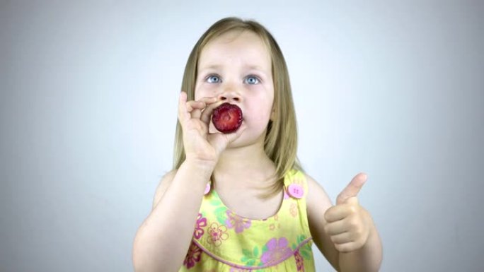 一个三岁的小女孩吃草莓，露出拇指。