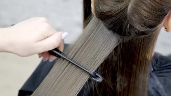 理发师在美容院为一个黑发女孩做头发层压。特写