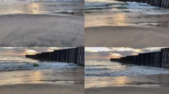 海滩和海浪的近景日落附近的国际边界墙在Playas Tijuana，墨西哥