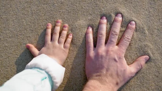 成人和儿童手在日落慢动作时在沙滩上留下手印